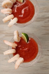 Photo of Tasty shrimp cocktail with sauce and lime in glasses on wooden table, flat lay