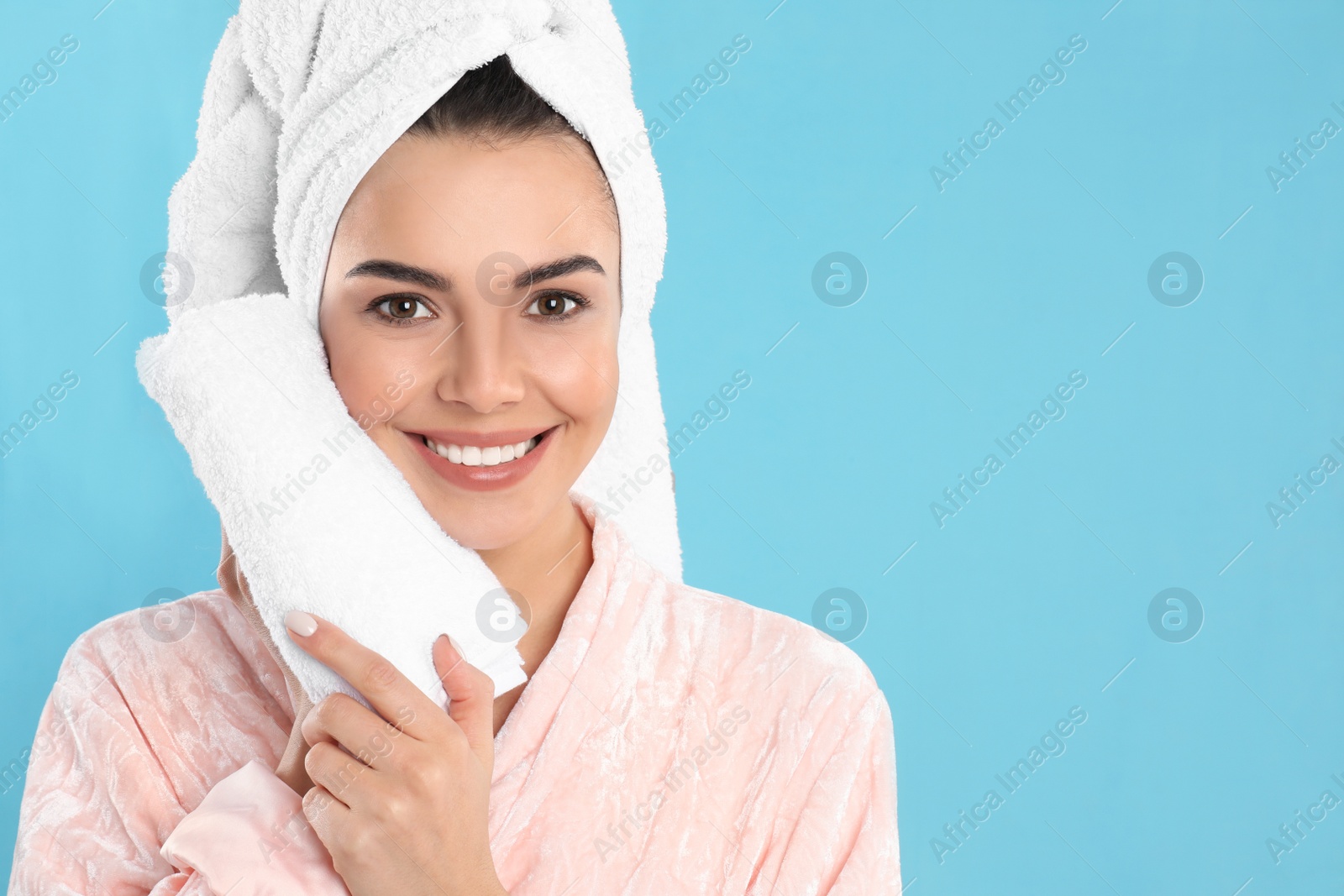 Photo of Young woman wiping face with towel on light blue background. Space for text