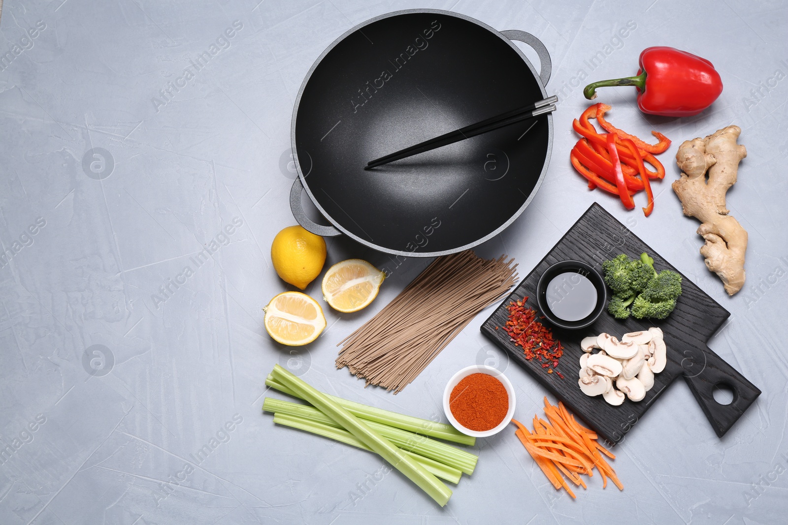 Photo of Wok, chopsticks and different products on grey table, flat lay. Space for text