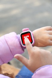 Little girl using SOS function on smartwatch outdoors, closeup