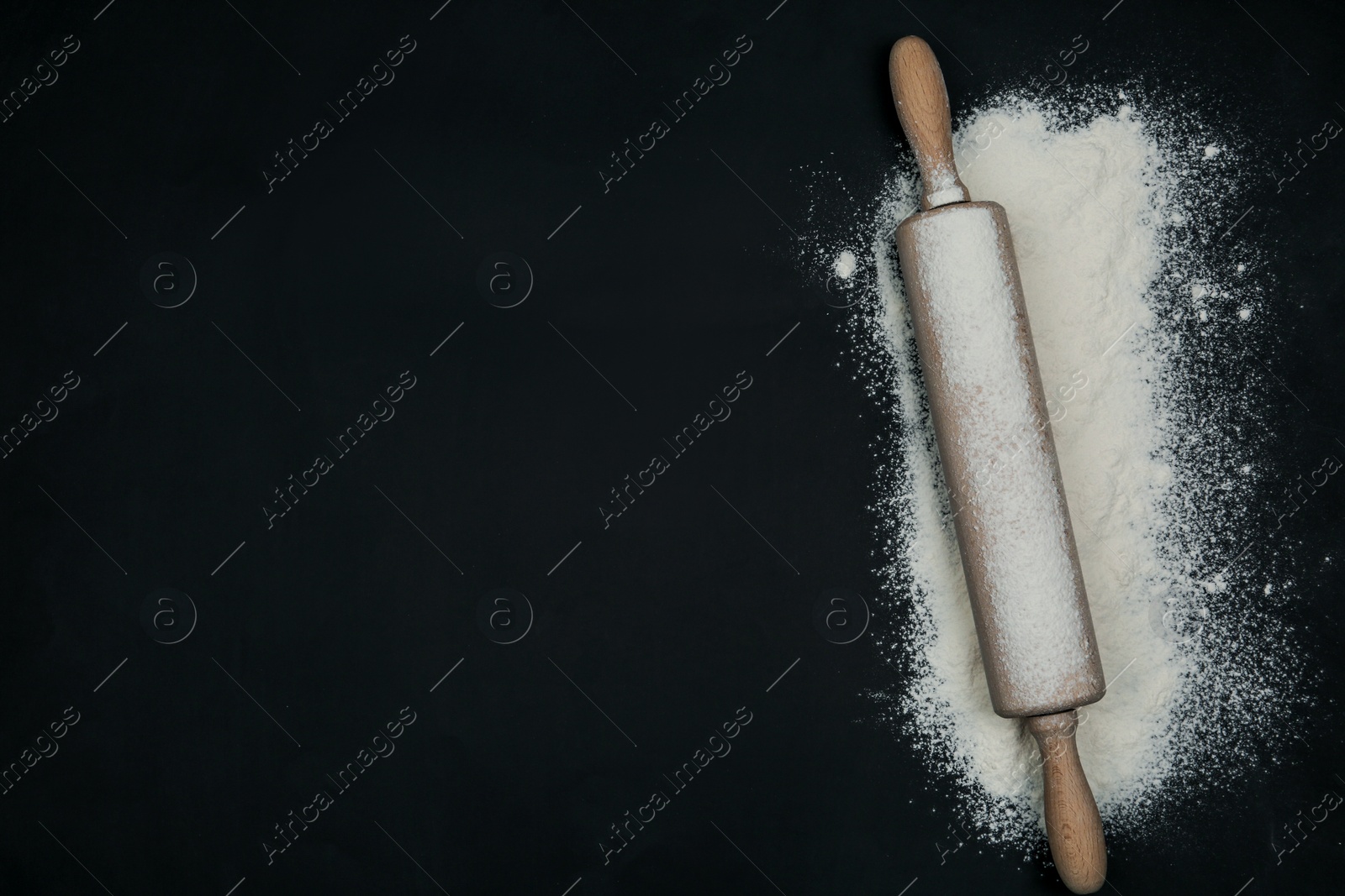 Photo of Flour and rolling pin on black table, top view. Space for text