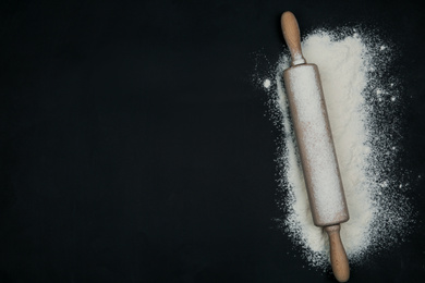 Flour and rolling pin on black table, top view. Space for text