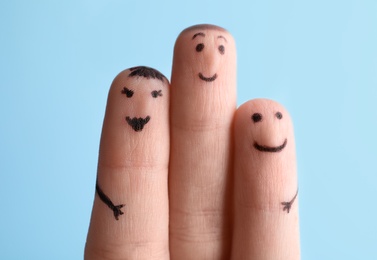 Photo of Three fingers with drawings of happy faces on light blue background