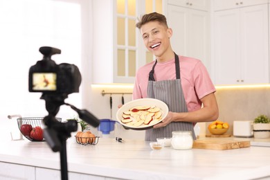 Photo of Smiling food blogger explaining something while recording video in kitchen