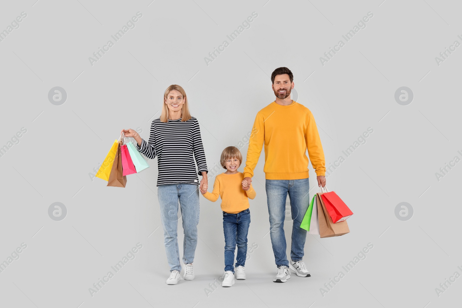 Photo of Family shopping. Happy parents and son with many colorful bags on light grey background