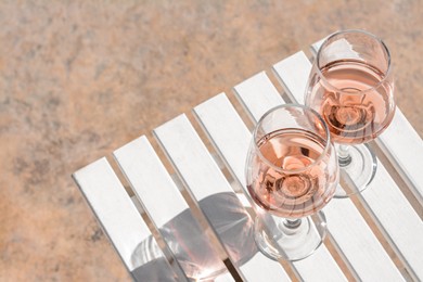 Photo of Glasses of tasty rose wine on white wooden table, space for text