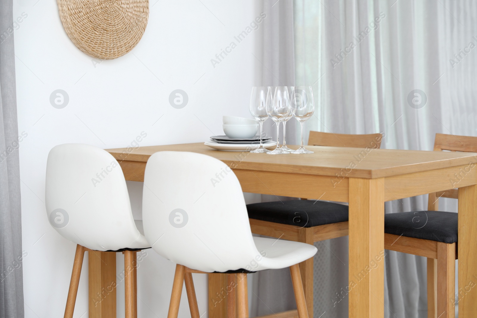 Photo of Stylish room interior with dining table and bar stools near white wall