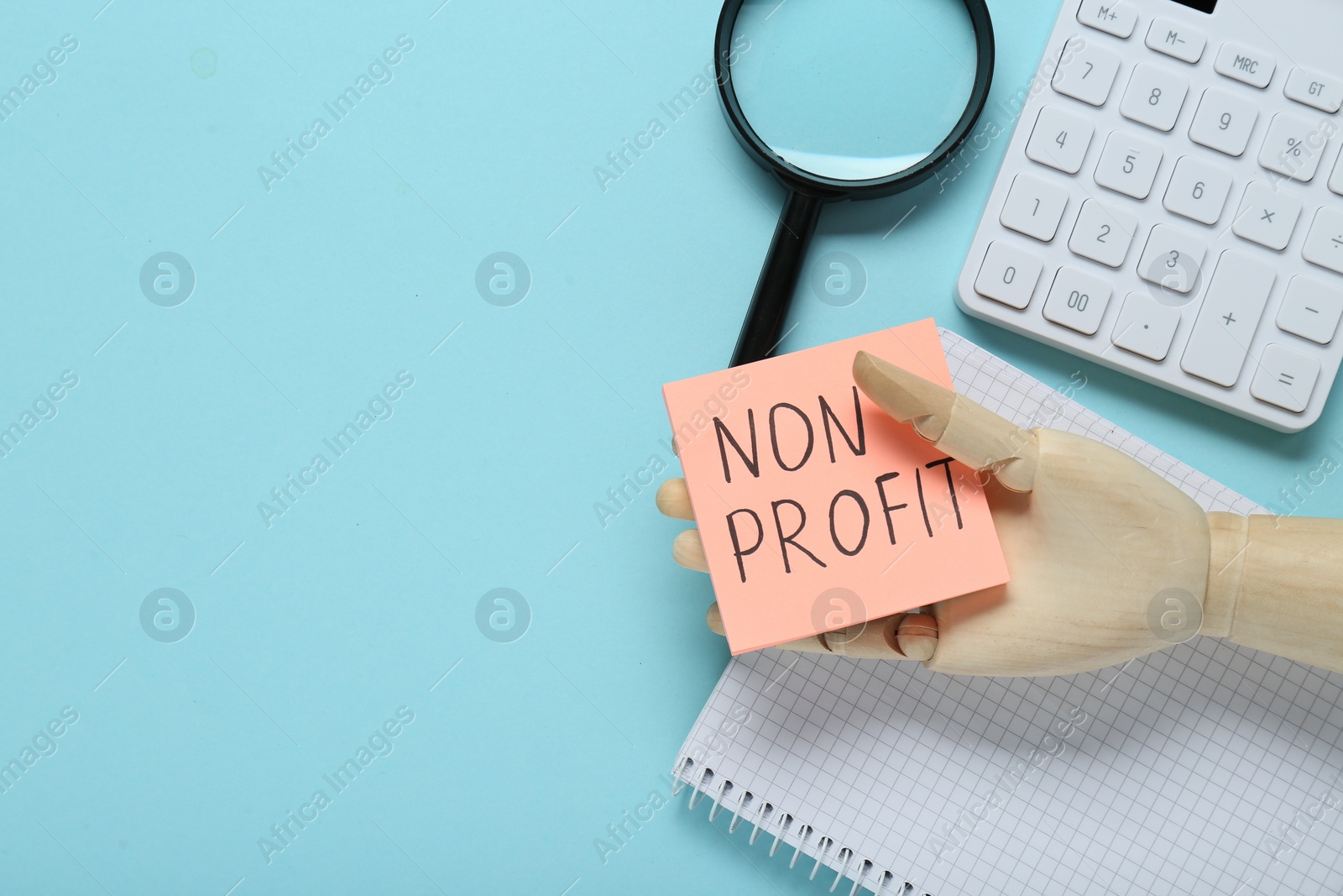 Photo of Non Profit concept. Flat lay composition with paper note in wooden mannequin hand on light blue background, space for text