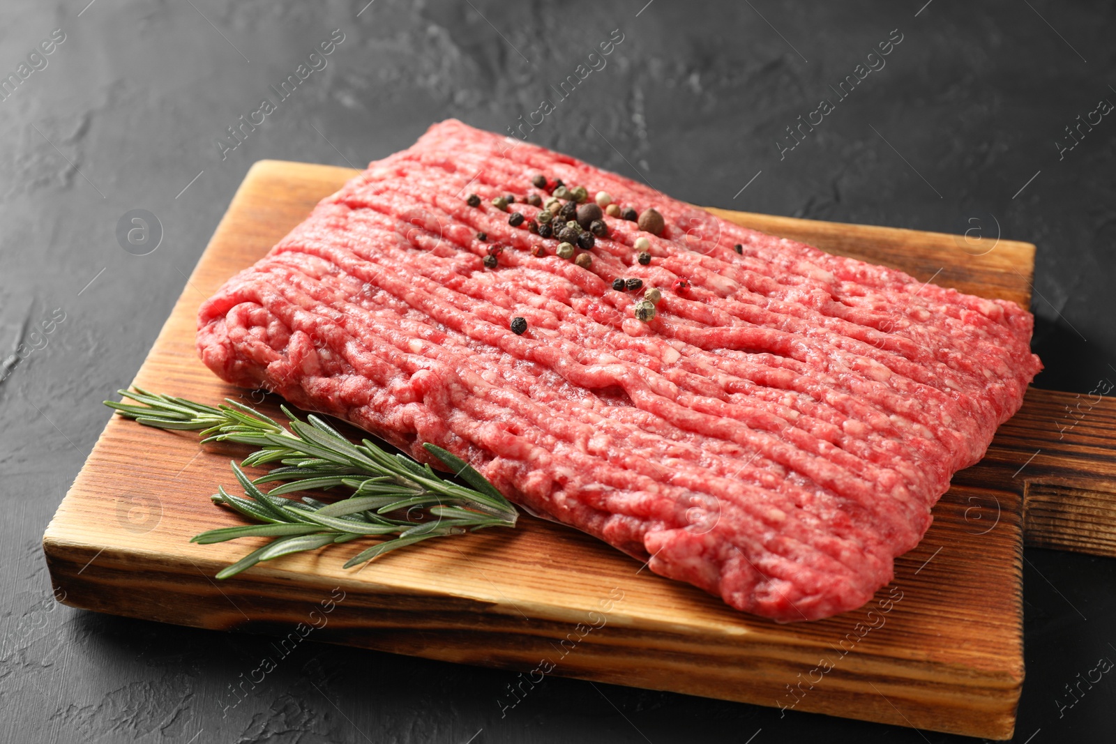 Photo of Raw ground meat, rosemary and peppercorns on black table