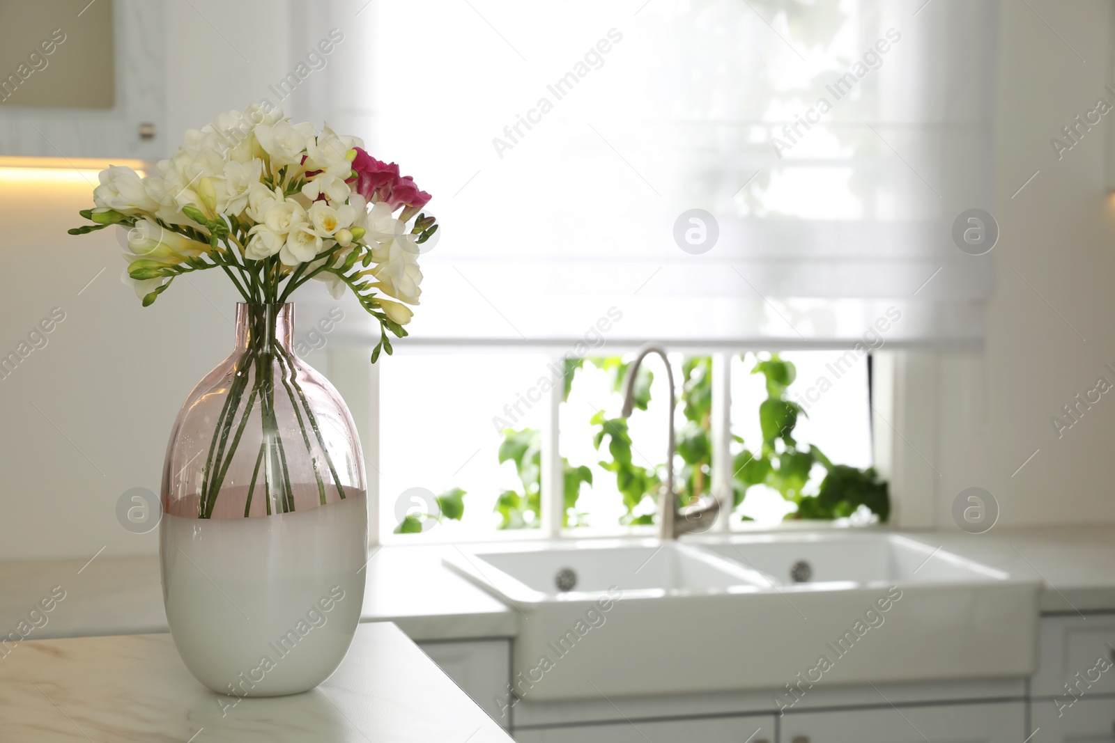 Photo of Beautiful bouquet of freesia flowers on countertop in kitchen. Space for text