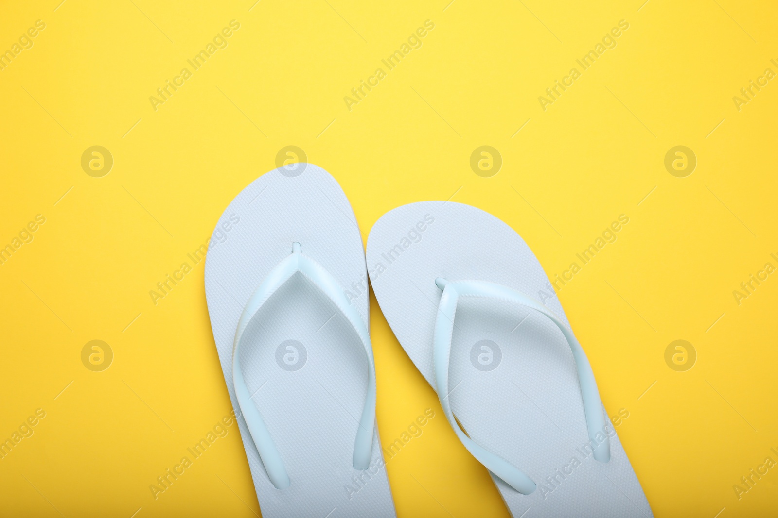 Photo of Stylish white flip flops on yellow background, top view