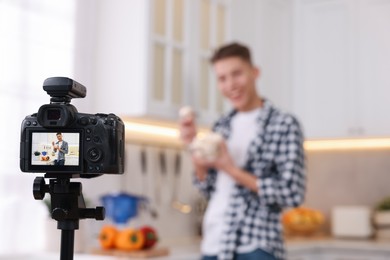 Photo of Food blogger recording video in kitchen, focus on camera