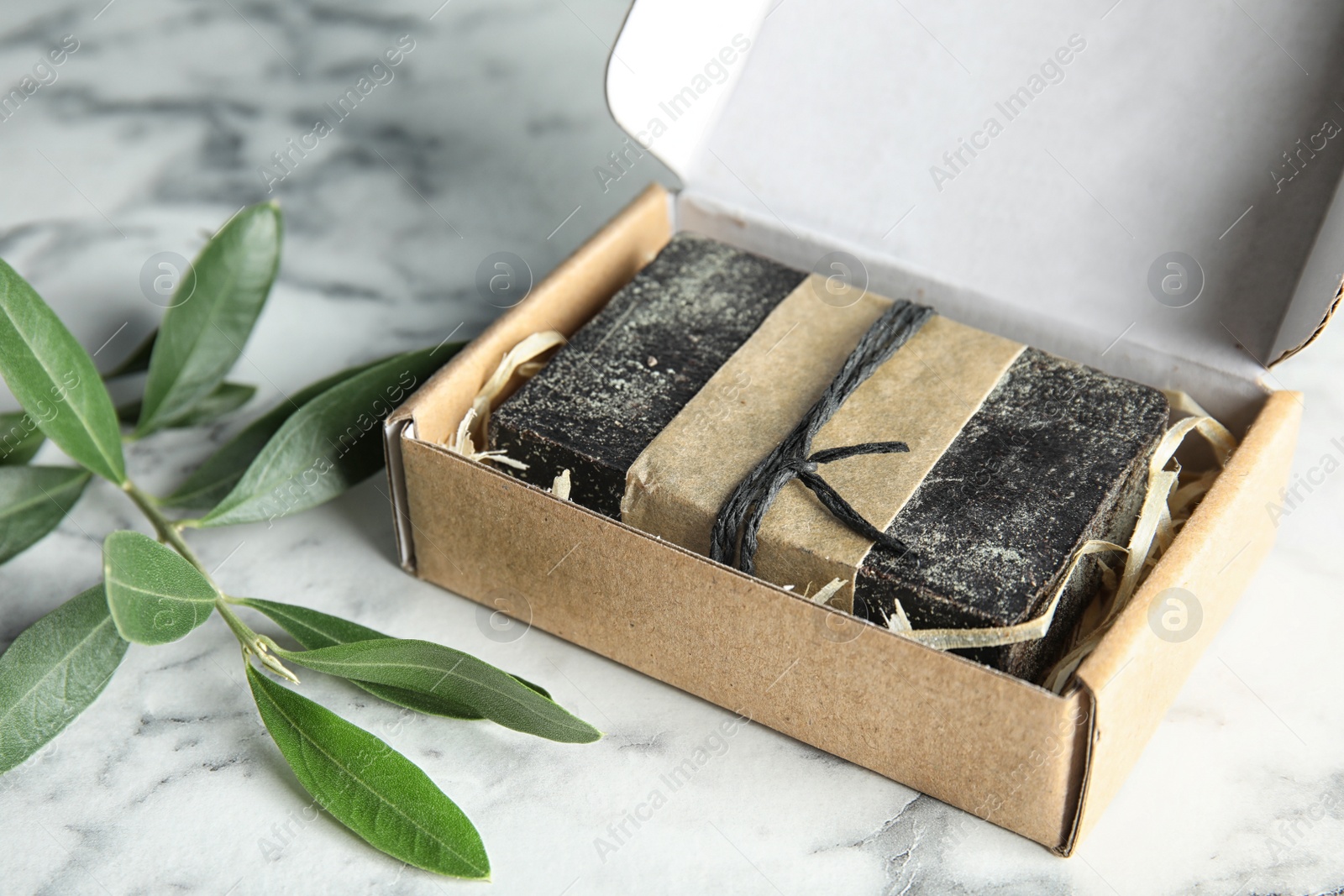 Photo of Handmade soap bar in cardboard box and olive twig on table