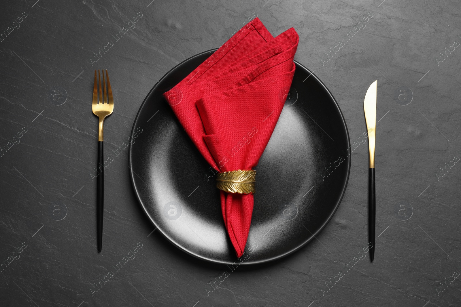 Photo of Plate with red fabric napkin, decorative ring and cutlery on black table, flat lay