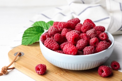 Photo of Bowl with delicious ripe raspberries on wooden cutting board, space for text