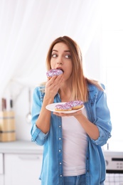 Emotional young woman eating donut in kitchen. Failed diet