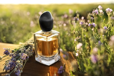 Photo of Bottle of luxury perfume and lavender flowers on wooden table in blooming field