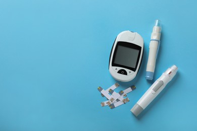 Photo of Digital glucometer, lancet pens and test strips on light blue background, flat lay with space for text. Diabetes control