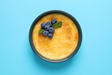 Photo of Delicious creme brulee with fresh blueberries and mint on light blue background, top view