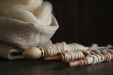 Photo of Soft white wool and spindles on wooden table, closeup