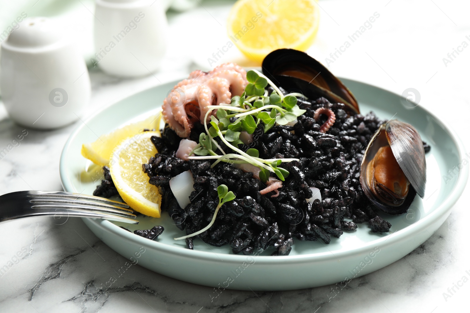 Photo of Delicious black risotto with seafood on white marble table