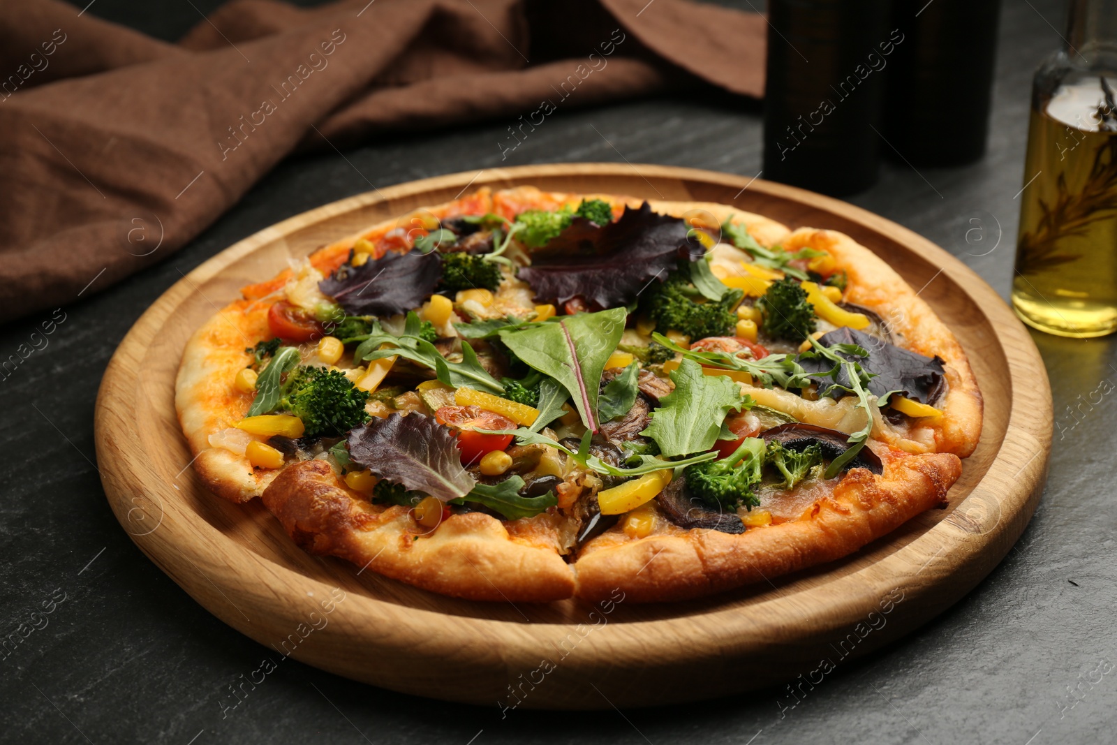 Photo of Delicious vegetarian pizza with mushrooms, vegetables and greens on black table