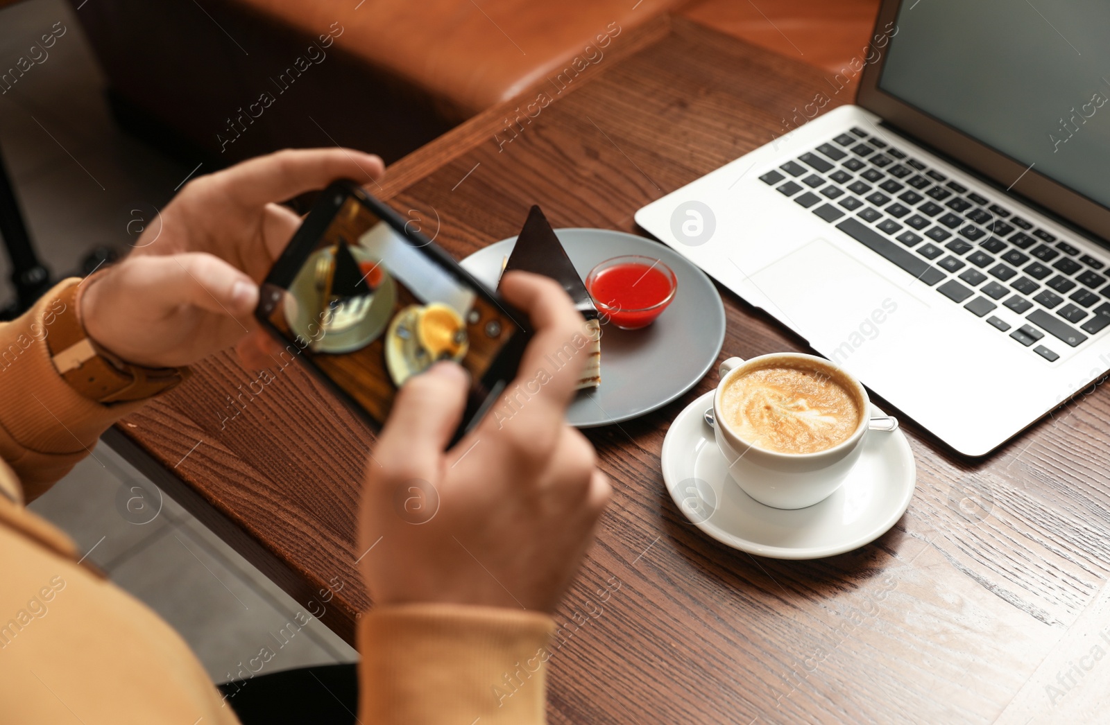 Photo of Male blogger taking photo of dessert and coffee at table in cafe, closeup