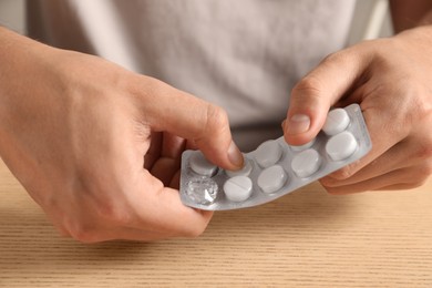 Photo of Man taking pill out from blister pack at wooden table, closeup