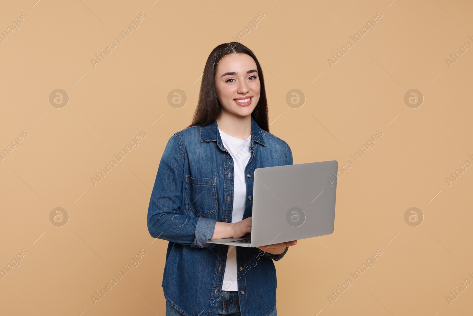 Photo of Smiling young woman working with laptop on beige background