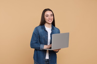 Smiling young woman working with laptop on beige background