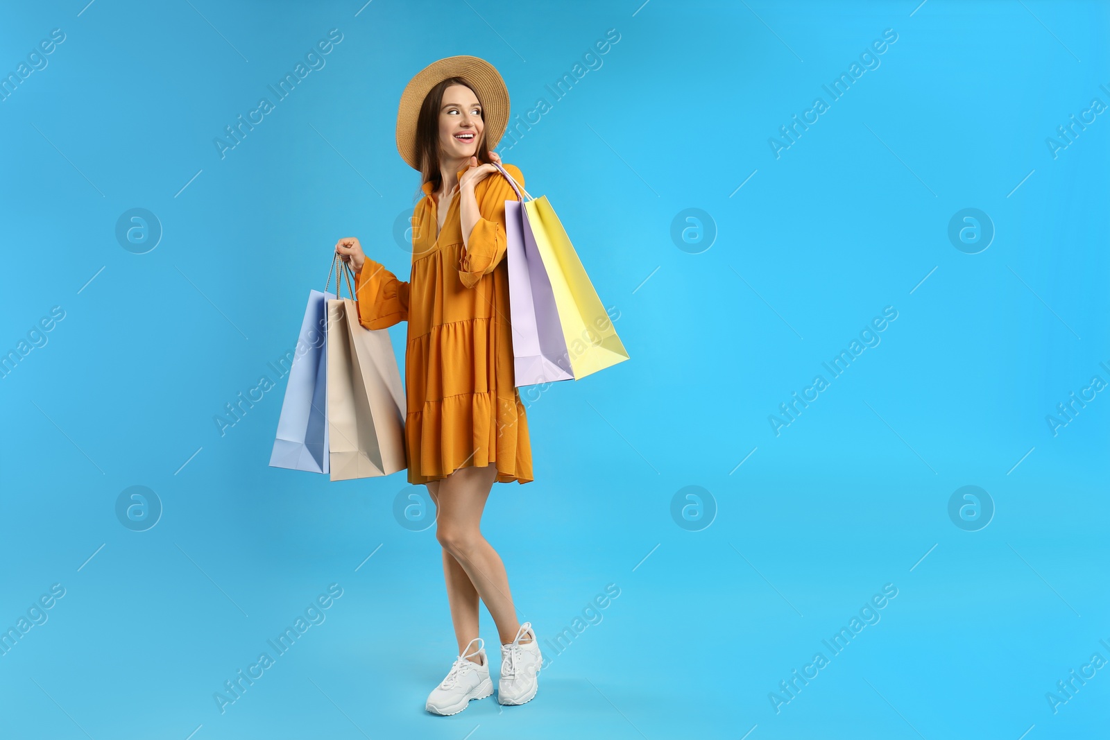 Photo of Beautiful young woman with paper shopping bags on light blue background