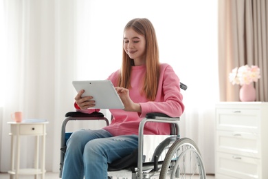 Teenage girl with tablet in wheelchair at home