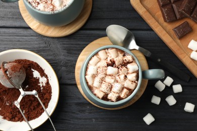 Photo of Cups of aromatic hot chocolate with marshmallows and cocoa powder served on dark gray wooden table, flat lay