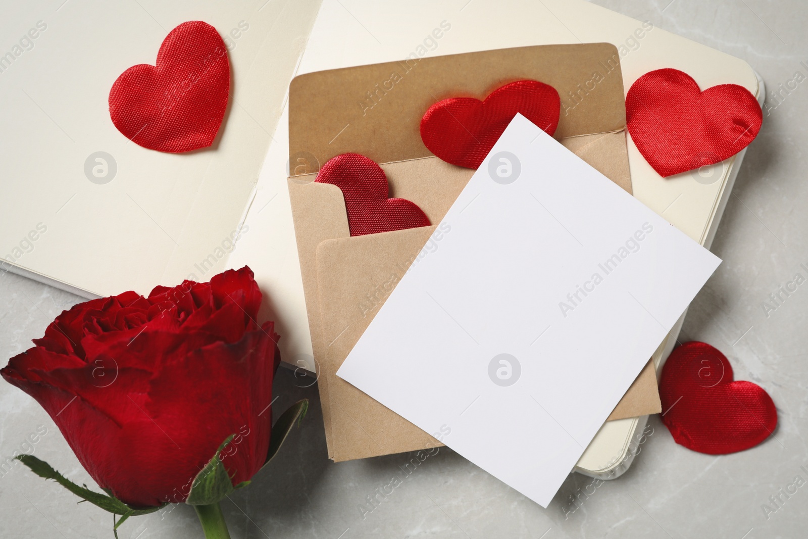 Photo of Composition with blank greeting card, rose and notebook on light grey marble table, above view. Valentine's day celebration