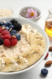 Photo of Tasty oatmeal porridge with berries, banana and chia seeds on light table, closeup