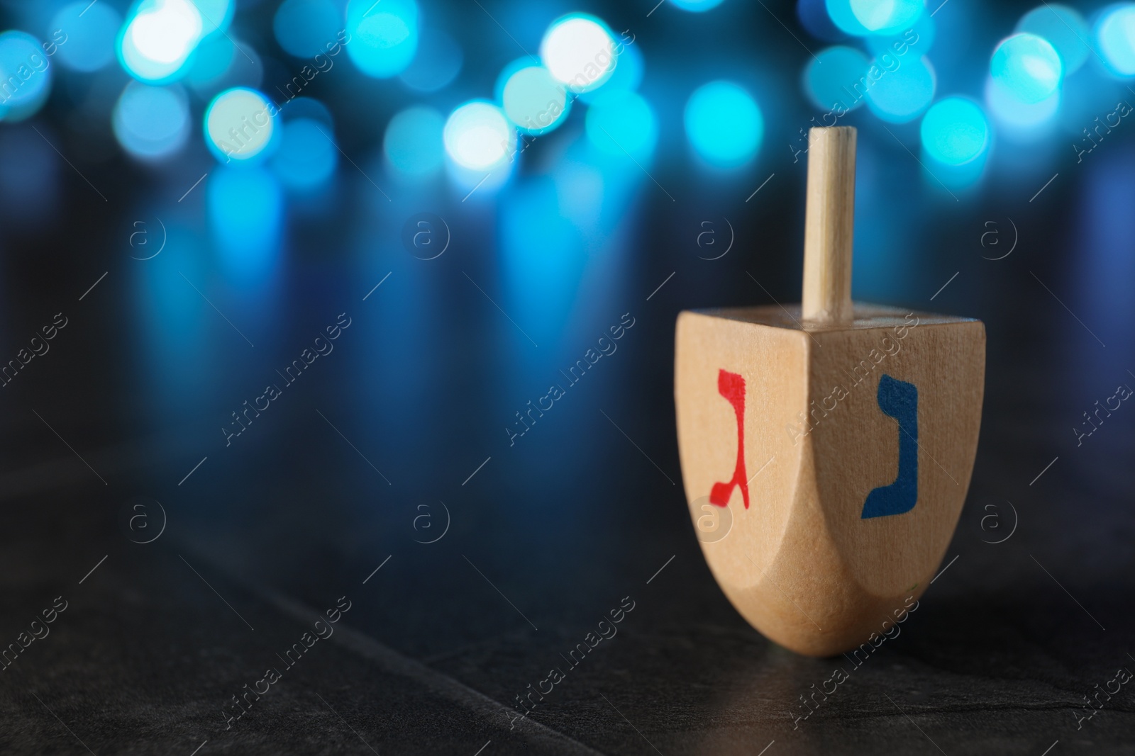 Photo of Hanukkah traditional dreidel with letters Gimel and Nun on table against blurred lights, closeup. Space for text