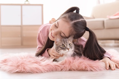 Photo of Cute little girl with cat lying on floor at home