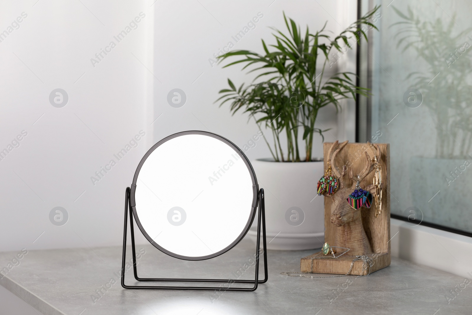 Photo of Mirror, holder with jewelry and houseplant on light grey stone window sill