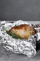 Photo of Tasty pork baked in foil and rosemary on grey textured table, space for text