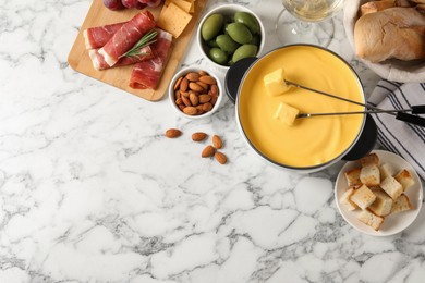 Photo of Pot of tasty cheese fondue and snacks on white marble table, flat lay. Space for text