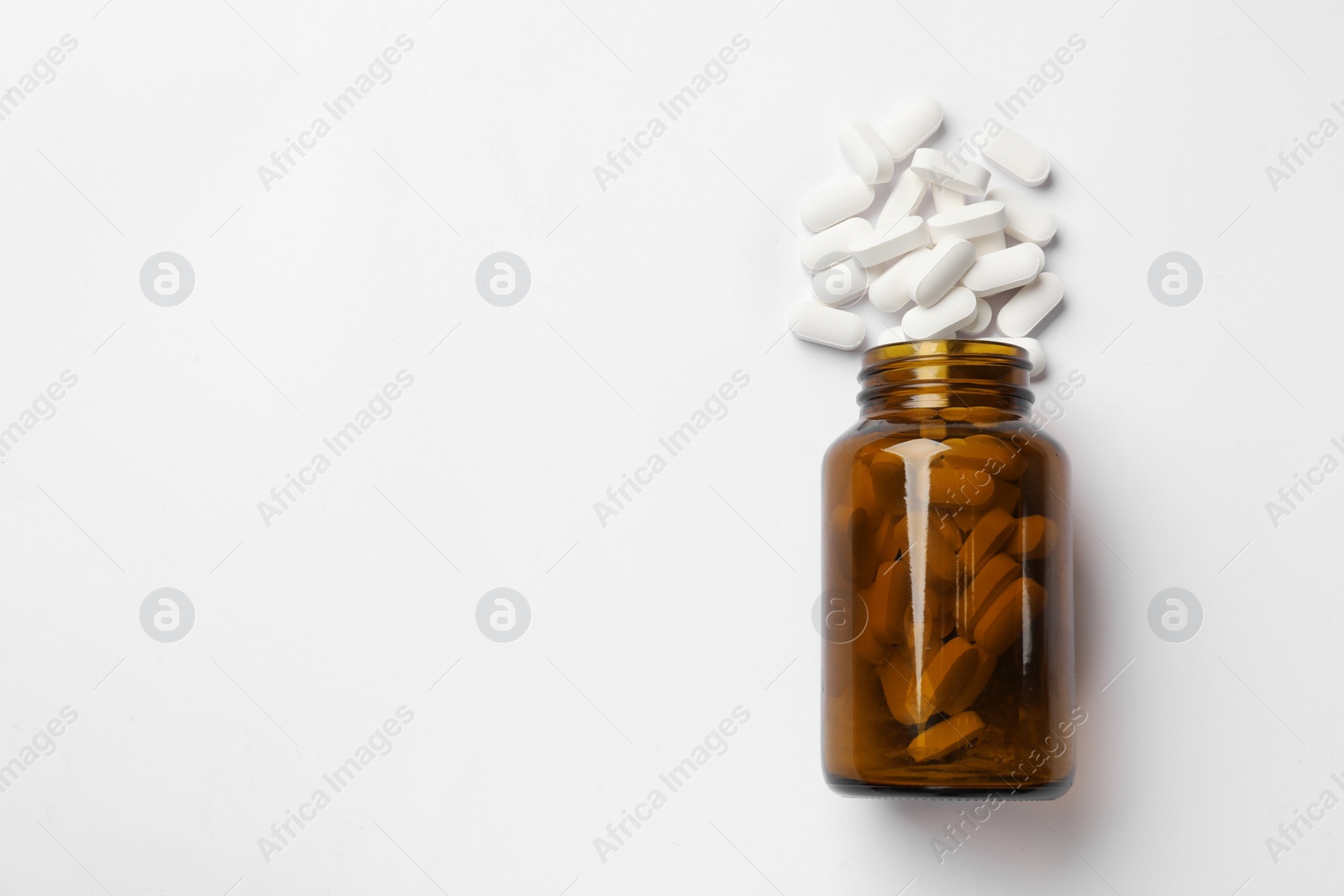 Photo of Vitamin pills and bottle on white background, top view. Space for text