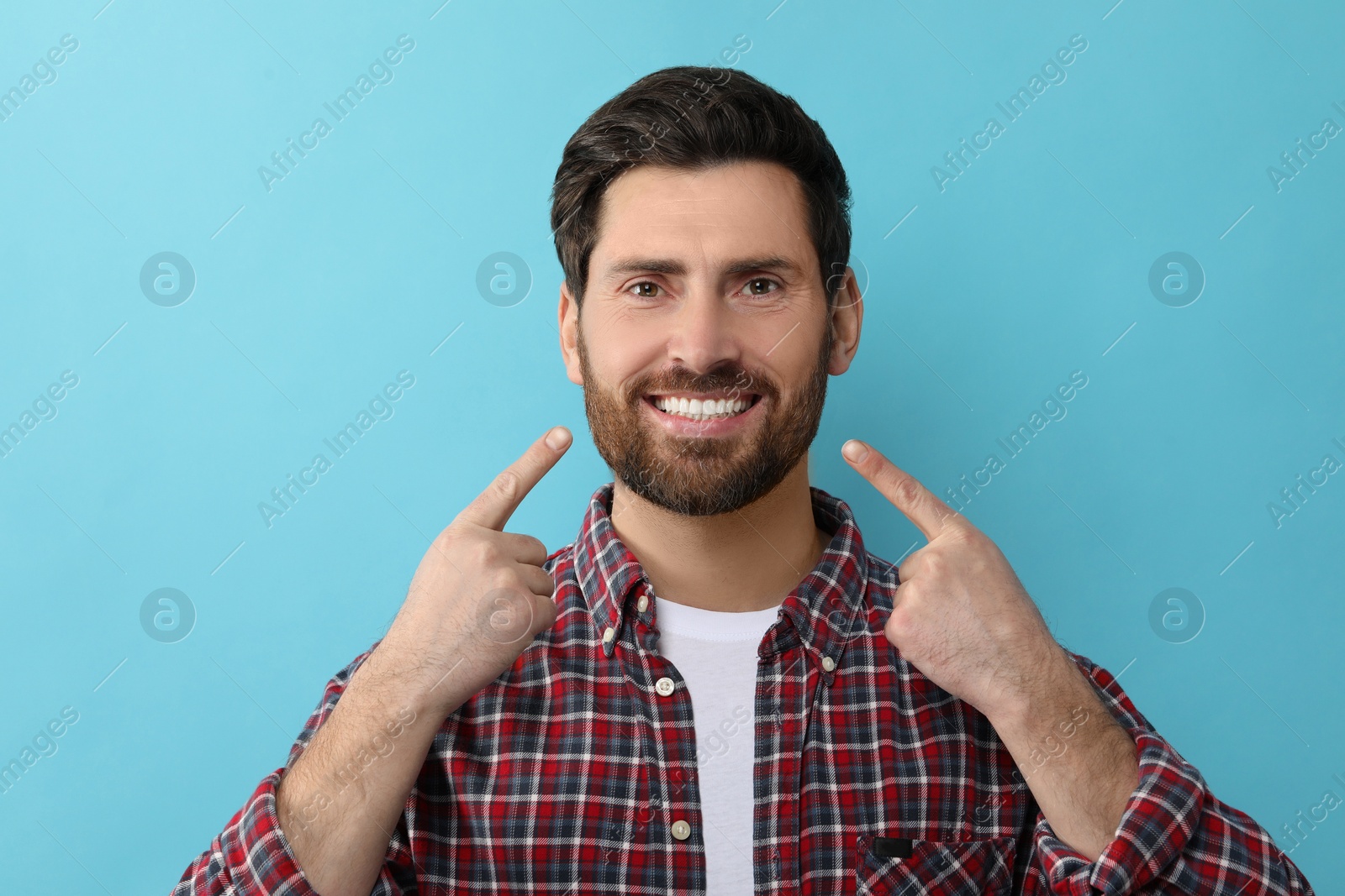 Photo of Smiling man pointing at his healthy clean teeth on light blue background