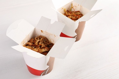 Photo of Chinese noodles in paper boxes on white wooden table. Food delivery