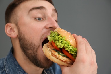 Photo of Young man eating tasty burger on grey background