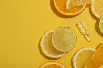 Photo of Skincare ampoules with vitamin C and citrus slices on yellow background, flat lay. Space for text