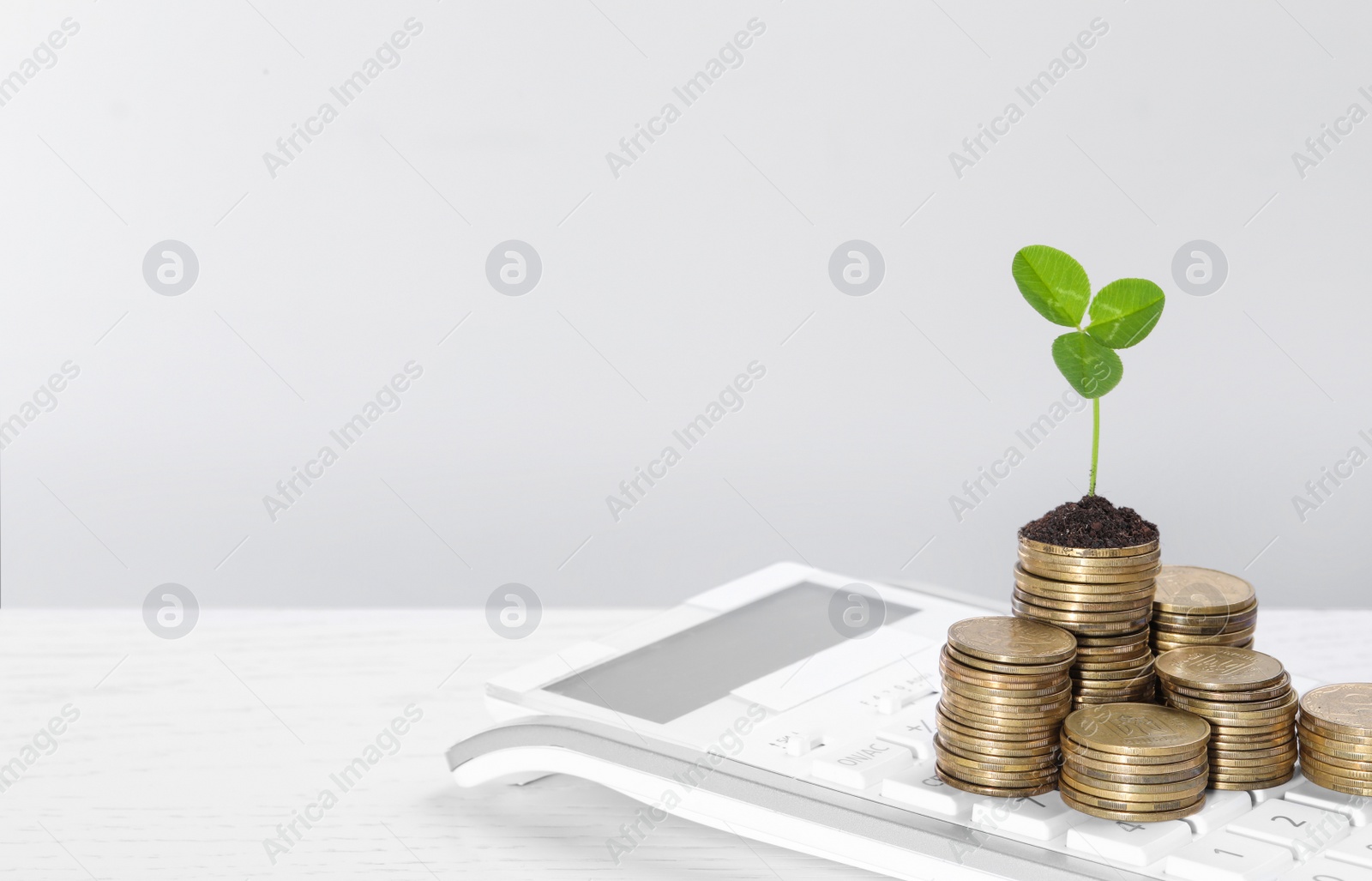 Photo of Stacks of coins with green sprout and calculator on white table, space for text. Investment concept