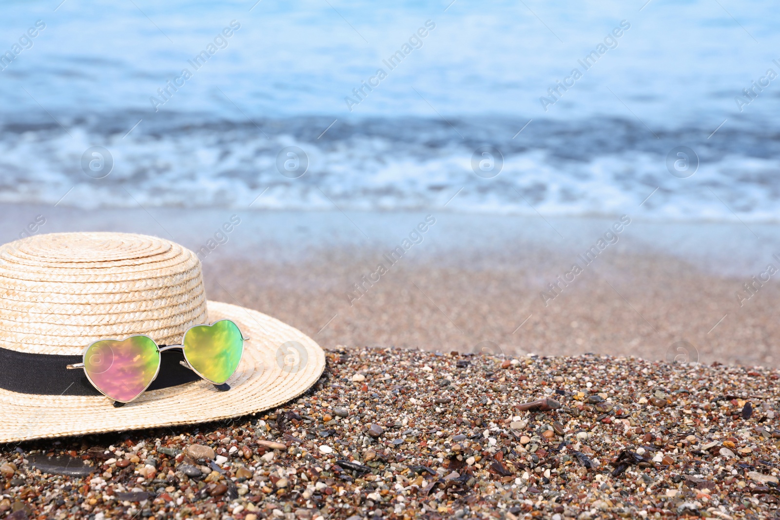 Photo of Straw hat and colorful heart shaped sunglasses on sea beach. Space for text