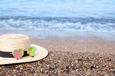 Photo of Straw hat and colorful heart shaped sunglasses on sea beach. Space for text