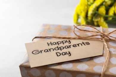 Photo of Gift box and tag with phrase Happy Grandparents Day on light background, closeup