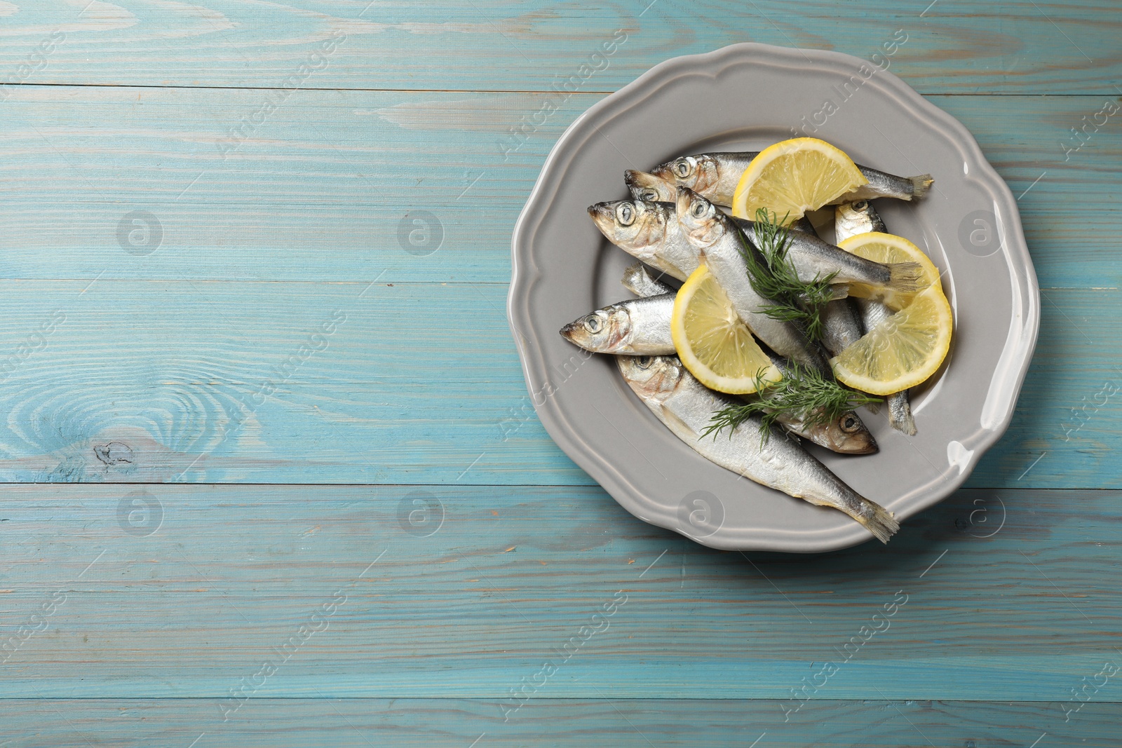 Photo of Fresh raw sprats, dill and cut lemon on light blue wooden table, top view. Space for text